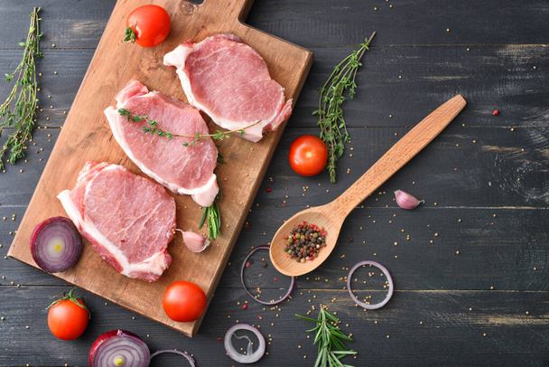 Board with raw pork meat, vegetables and spices on dark wooden background - Foto, afbeelding