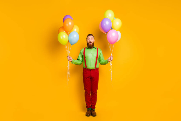 Full length photo of astonished imposing charming man hipster go party hold many baloons impressed festive event scream wow omg wear stylish clothing isolated over yellow color background - Fotó, kép