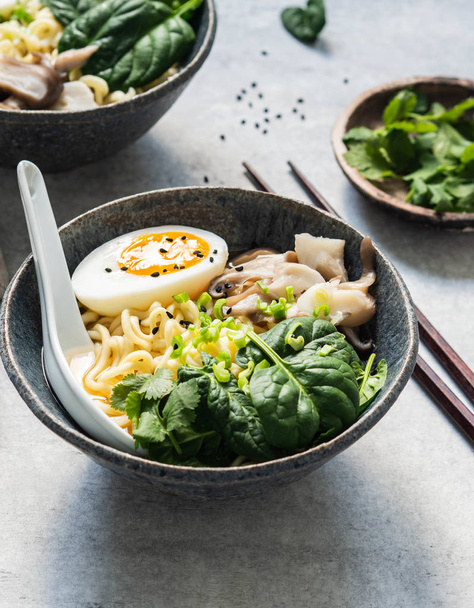 Miso Ramen vegetariano con funghi, spinaci crudi e uova sode in ciotola blu su tavola grigia
 - Foto, immagini