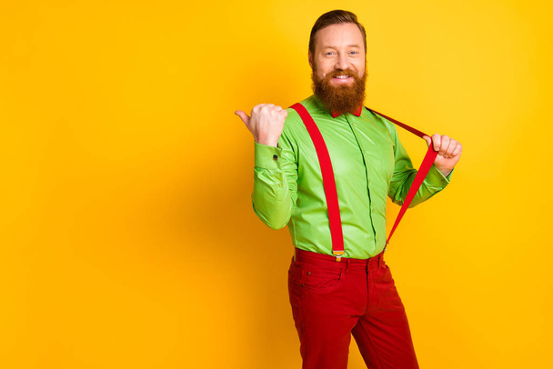 Photo of attractive funny guy cool funky look indicating thumb finger empty space sale shopping wear green shirt red bow tie suspenders pants isolated vivid color background - Foto, Imagen