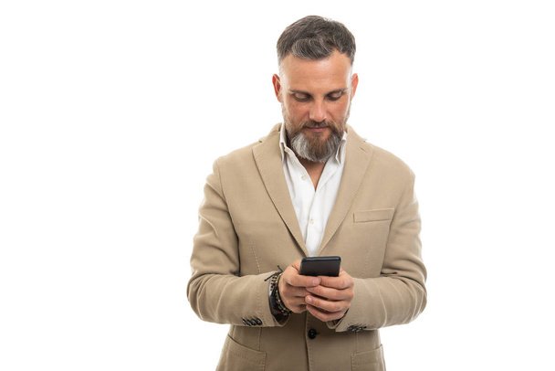 コピースペース広告エリアと白い背景に隔離されたスマートフォンにスマートカジュアル服のテキストメッセージを身に着けている男 - 写真・画像