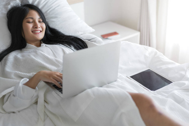 Young woman working on a laptop sitting on bed at home. - Photo, Image