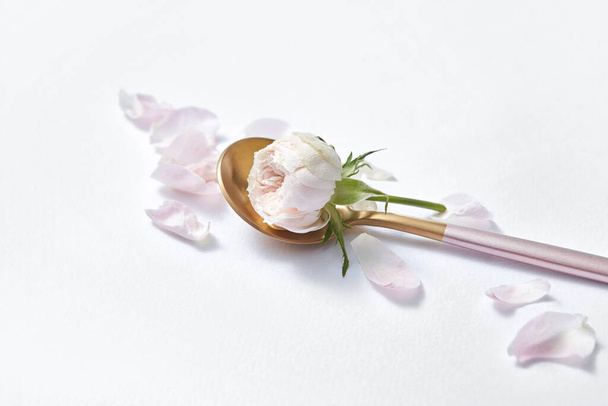 Natural organic fresh pink rose flower in the golden dessert spoon with tender petals on a light grey background, copy space. Valentine's day greeting card. - Zdjęcie, obraz