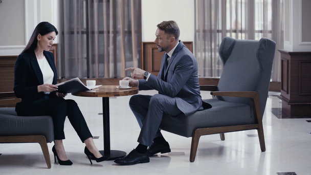 ビジネスパートナーはコーヒーを飲み、レストランロビーで紙と仕事をする - 映像、動画