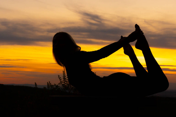 Silhueta mulher treinador prática de ioga ao pôr do sol. Conceito de ioga. Bow Pose. Dhanurasana
 - Foto, Imagem