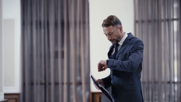 Hombre de negocios con documentos mirando el reloj de pulsera en el vestíbulo del restaurante
 - Metraje, vídeo
