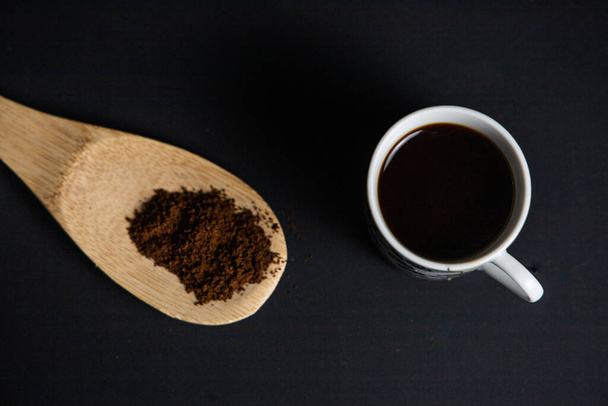 Musta kahvi puinen lusikka ja jauhettua kahvia mustalla taustalla näkymä
 - Valokuva, kuva
