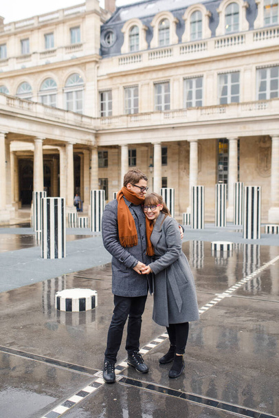 Young beautiful couple dressed stylishly, a girl in a gray coat, a man in a gray coat stand on a square in Paris France - Φωτογραφία, εικόνα