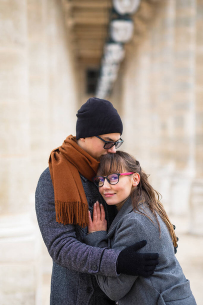 Young beautiful couple dressed stylishly, a girl in a gray coat, a man in a gray coat stand on a square in Paris France - Φωτογραφία, εικόνα