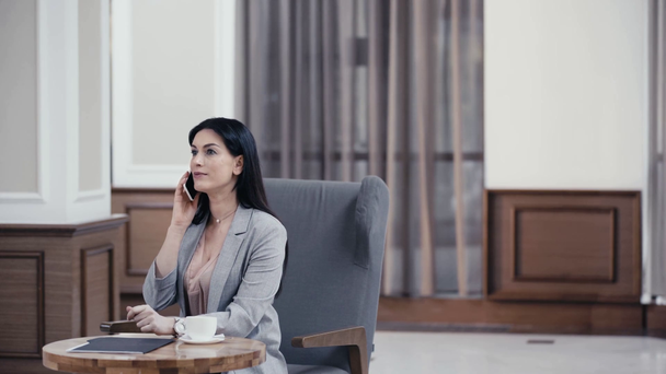 Bizneswoman rozmawia na smartfonie i pije kawę w lobby restauracji - Materiał filmowy, wideo
