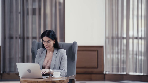 Bizneswoman z kawą posiadające połączenie wideo na laptopie w lobby restauracji - Materiał filmowy, wideo