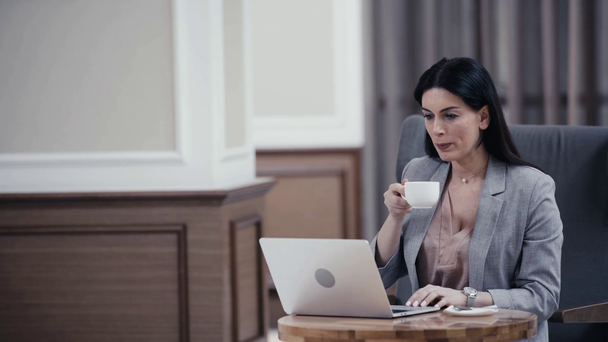 Businesswoman drinking coffee and using laptop in lobby of restaurant - Metraje, vídeo