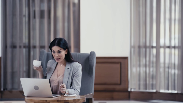 Деловая женщина с кофе с видеозвонком на ноутбуке в вестибюле ресторана
 - Кадры, видео