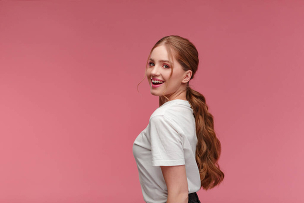 Beauty portrait of smiling redhead girl. Perfect skin. Beautiful female model with long hair over pink background. Young cute woman with clear skin. Skincare and facial treatment concept - Zdjęcie, obraz