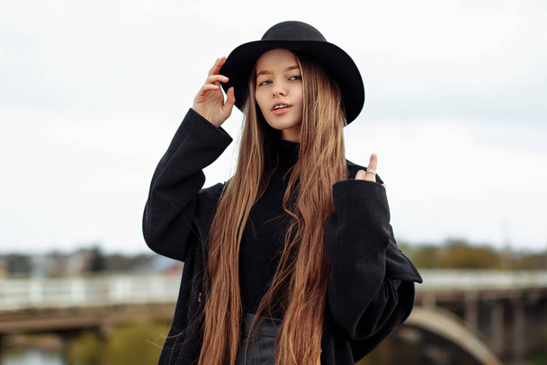 Fiatal, gyönyörű, divatos nő fekete kalapban, hosszú hajjal. Női divat, szépség koncepció. Kültéri. - Fotó, kép