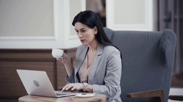 İş kadını kahve içiyor ve restoranın lobisinde dizüstü bilgisayar kullanıyor. - Video, Çekim