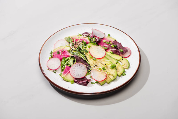 fresh radish salad with greens and avocado on grey surface - Фото, зображення