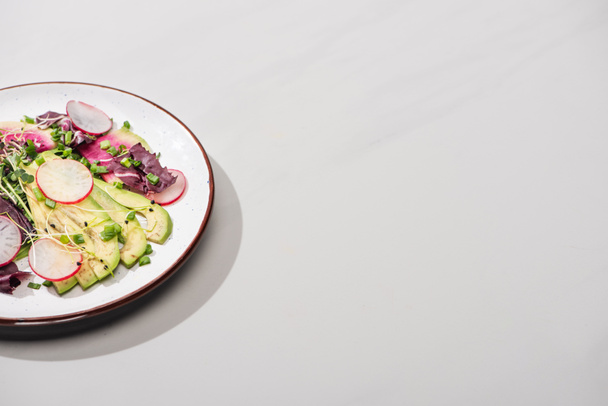 fresh radish salad with greens and avocado on grey surface - Фото, изображение