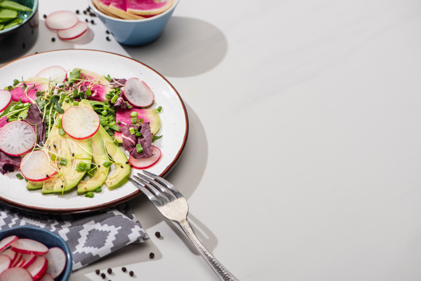 fresh radish salad with greens and avocado on grey surface with napkin and fork - Fotoğraf, Görsel