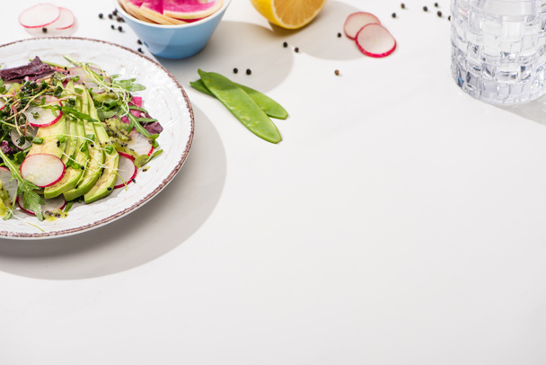 ensalada de rábano fresco con verduras y aguacate en la superficie blanca con ingredientes en cuencos y agua
 - Foto, Imagen