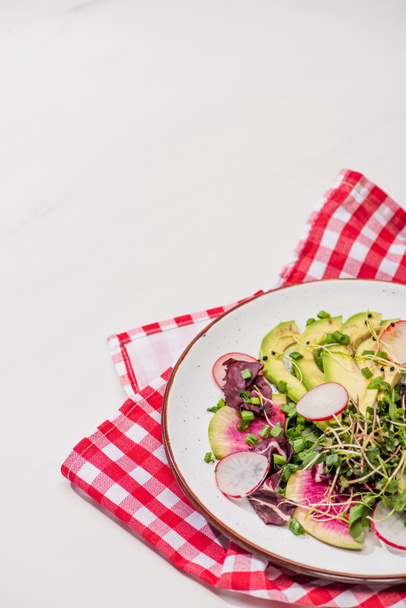 fresh radish salad with greens and avocado on plate on white surface with napkin - Фото, зображення