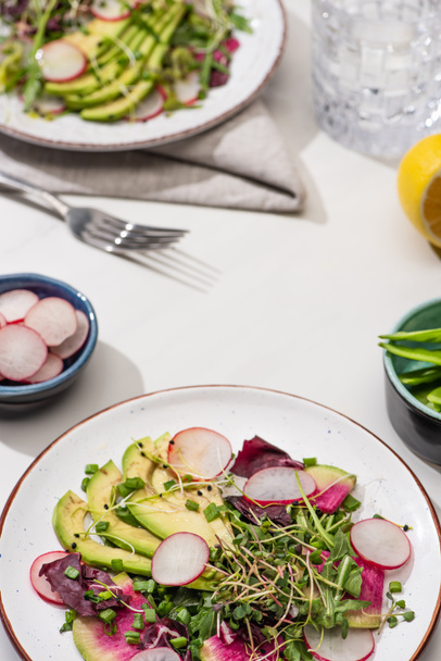 selective focus of fresh radish salad with greens and avocado on white surface - Фото, зображення