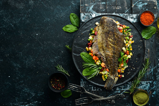 Baked Flounder Fish with Vegetables on a Black Stone Plate. Seafood. Top view. Free space for your text. - Zdjęcie, obraz