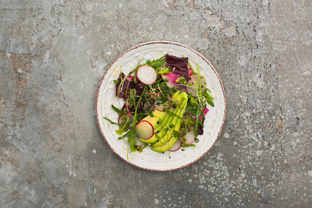 top view of fresh radish salad with greens and avocado on grey concrete surface - 写真・画像