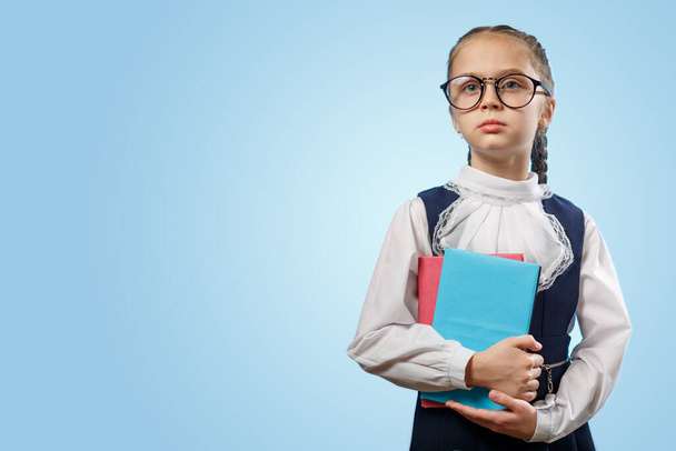 Aranyos iskoláslány szemüvegben tartsa könyvek Másolat. Okos kaukázusi diáklány visel hagyományos iskolai egyenruha kék háttér. Elemi tanuló plázákkal Nézz félre nevelési koncepció - Fotó, kép