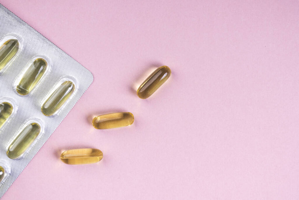 Olie gele capsules op roze achtergrond, vitaminen en antioxidant concept Omega 3, lever kabeljauw of 's avonds primose olie voor de gezondheidszorg. Minimalisme. Kopieerruimte. - Foto, afbeelding