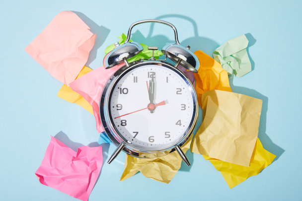 top view of classic alarm clock with crumpled colorful sticky notes on blue background - Photo, Image