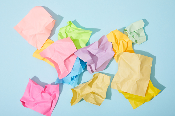 top view of crumpled colorful sticky notes on blue background - 写真・画像