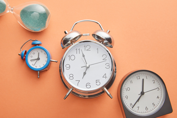 top view of alarm clocks and hourglass on peach background - Foto, afbeelding