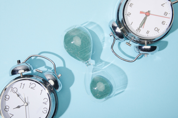 top view of classic alarm clocks and hourglass on blue background - Foto, afbeelding
