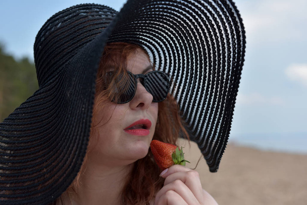 portrait of a woman in a wide-brimmed hat and sunglasses with strawberries in her hands - Фото, зображення