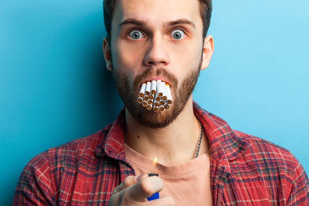 Shocked adult man with cigarettes in his mouth isolated on blue background - Photo, image