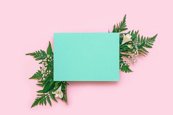 Creative layout made of flowers and leaves with paper card on pink background. - Foto, imagen