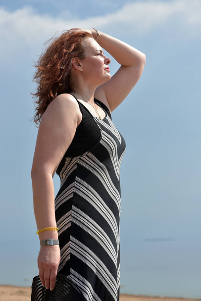 woman in a striped dress on a background of the sea with a hat in her hands - Foto, immagini
