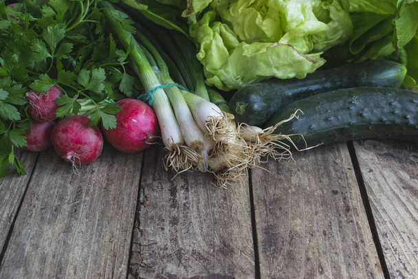 Organická, jarní zelenina (ředkvička, jarní cibule, salát, okurka) na starém dřevěném stole s kopírovacím prostorem - Fotografie, Obrázek