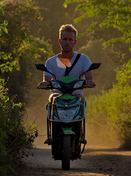 Bagan. Myanmar. 25. listopadu2016. Mladý muž na motorce projíždí zaprášenou cestou v obrysovém světle spěchá do úžasných buddhistických chrámů Baganu, aby viděl zářící západ slunce. - Fotografie, Obrázek