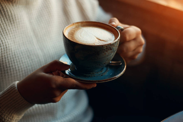 Hands of man holding a black cup of hot latte indoors - Fotoğraf, Görsel