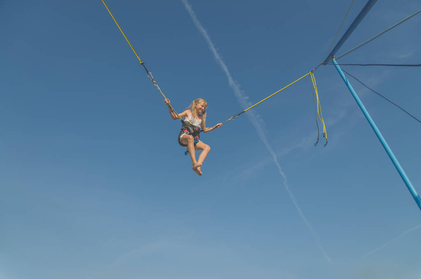 activa niña adolescente saltando en trampolín alto en el cielo azul safed con cinturón de seguridad elástico - Foto, imagen