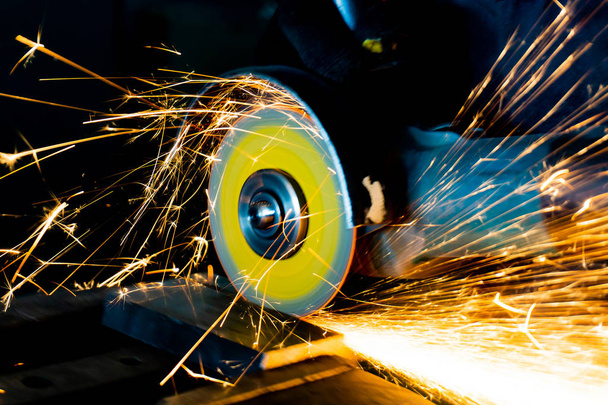 The worker cuts the part with an angle grinder, the abrasive wheel produces sparks when cutting - Photo, Image