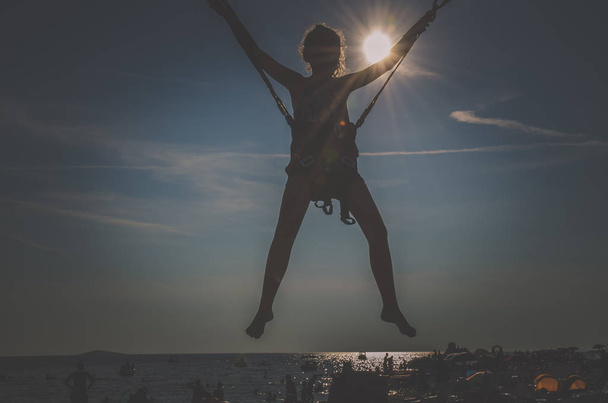 silhouette of girl enjoying adrenaline sporty activity in bungee jumping construction at the seaside - Photo, Image