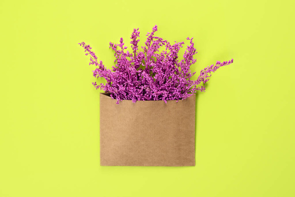 明るい緑の背景に隔離されたコピースペースを持つクラフト茶色の封筒内の明るい紫色または紫色の花。バレンタインデーや国際女性デーのためのトレンディなバナー . - 写真・画像