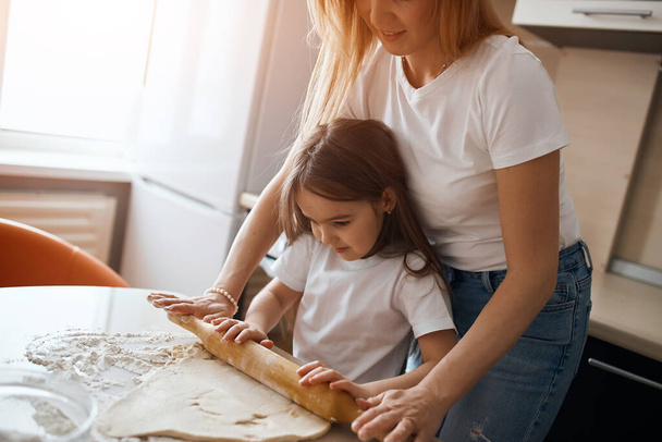 hardworking attractive girl helping her mother to bake a pie - Фото, изображение