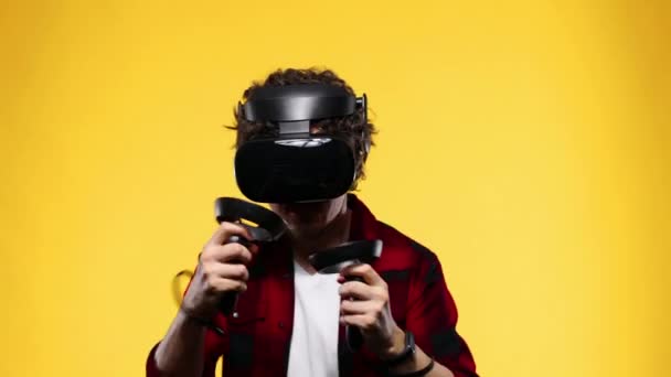 Young man with curly hair using a VR headset and experiencing virtual reality isolated on yellow background - Felvétel, videó