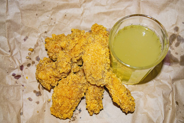 Хлебные куриные крылышки и стакан лимонада на сером бумажном фоне. Закрыть
 - Фото, изображение