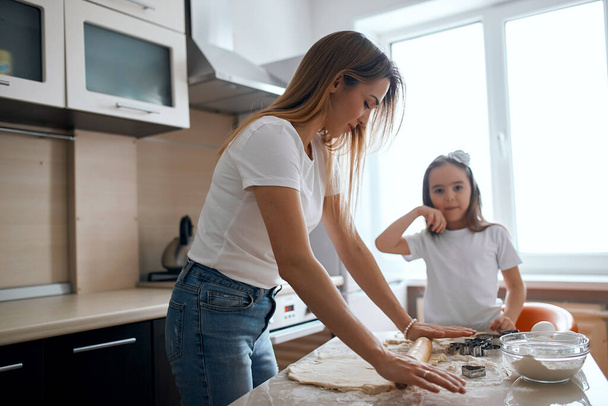 young fair-haired woman teaching her daughter to roll the dough - Φωτογραφία, εικόνα