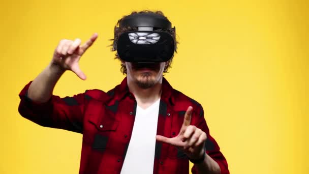Young man with curly hair using a VR headset and experiencing virtual reality isolated on yellow background - 映像、動画
